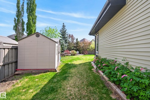 Expansive side yard featuring a plastic storage shed, manicured lawn, and a planted garden bed with blooming foliage - 2696 Anderson Crescent, Edmonton, AB - Outdoor With Exterior