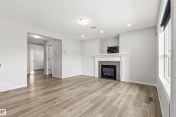 Spacious living area featuring wood-finish flooring, a contemporary fireplace with a white mantel and tiled surround, multiple recessed lights, a large window, and a ceiling-mounted light fixture - 