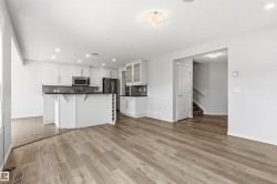 Open-concept living area featuring wood-finish flooring, a contemporary kitchen with white cabinetry, stainless steel appliances, a dark countertop, and a tiled backsplash - 