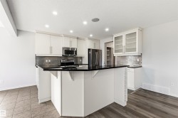 Contemporary kitchen featuring white cabinetry, dark countertops, a mosaic tile backsplash, and recessed lighting - 