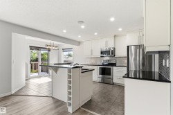 Modern kitchen featuring white cabinetry, stainless steel appliances, black countertops, and a tile backsplash - 