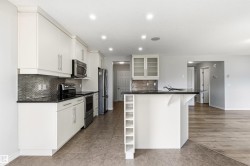 Contemporary kitchen featuring white cabinetry, black countertops, stainless steel appliances, and a mosaic tile backsplash - 