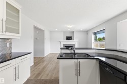 Contemporary kitchen featuring white cabinetry, black countertops, and a stainless steel sink with a single-lever faucet - 