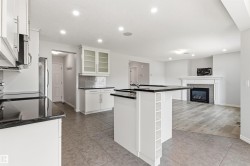 Open-concept kitchen and living area featuring white cabinetry, dark countertops, a kitchen island with built-in storage, and recessed lighting - 