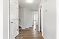 Neutral-toned hallway featuring wood-finish flooring, white trim, and a white interior door with polished hardware - 