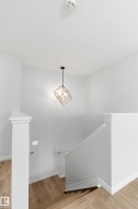 Stairwell featuring wood-finish flooring, white banister, and a contemporary geometric pendant light fixture - 