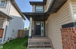Property exterior featuring a prominent black entry door with sidelights, beige horizontal siding, and a brick accent column - 
