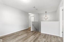Open concept loft space featuring wood-finish flooring, a modern geometric pendant light fixture, white trim, and a bright, neutral color palette - 