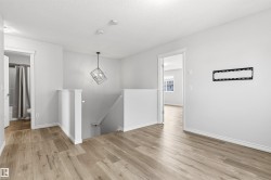 Upper-level landing featuring wood-finish flooring, white baseboards, and a contemporary geometric pendant light fixture - 