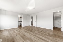 Spacious room featuring wood-finish flooring, a built-in closet system with shelving and drawers, a flush-mount ceiling light, and an integrated ceiling speaker - 