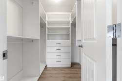 Walk-in closet with integrated shelving, multiple hanging rods, four built-in drawers with modern pulls, recessed lighting, and wood-finish flooring - 