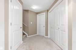 Carpeted hallway featuring a white bi-fold closet, additional white paneled doors, and a staircase with a matching white handrail - 