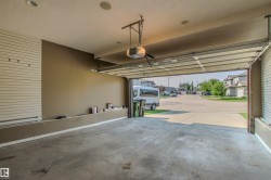 Spacious attached garage featuring concrete flooring, an automatic garage door opener, recessed lighting, slatwall organization system, and built-in shelving - 
