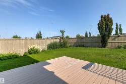 Expansive backyard featuring a wood-finish deck, lush green lawn, mature trees, and a privacy fence - 