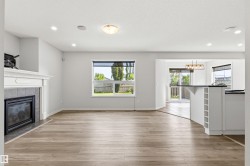 Open-concept living area featuring wood-finish flooring, a fireplace with a white mantel and tiled surround, recessed lighting, and a breakfast bar with built-in storage - 