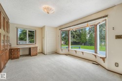 Spacious room featuring a large bay window overlooking a green yard, built-in desk with drawers, extensive wood-paneled cabinetry, and light-colored carpeting - 