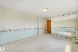 Carpeted room featuring a ceiling-mounted light fixture, full-height mirrored closet doors, and wood-trim windows - 