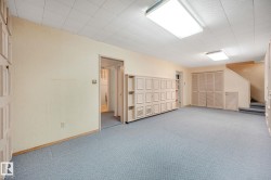 Spacious interior room featuring light blue carpeting, a drop ceiling with recessed lighting, and built-in white cabinetry - 
