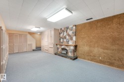 Spacious room featuring a stone-clad fireplace with a wood mantel, light blue carpeting, and built-in cabinetry - 