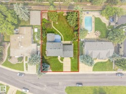 Aerial overview showcasing a substantial property with extensive green space, a paved driveway, and mature landscaping - 