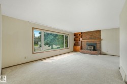 Living area featuring a large picture window, a brick fireplace with a wood-burning insert, and built-in wood shelving with cabinetry - 