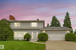 Two-story residence featuring light-colored siding, a prominent brick chimney, and a two-car garage with overhead lighting - 