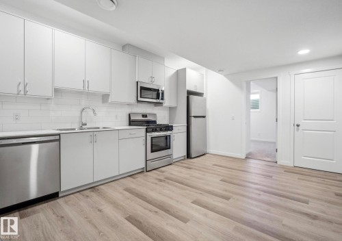 Full kitchen featuring white cabinetry, subway tile backsplash, stainless steel appliances, and light wood-finish flooring - 3888 Wren Crescent, Edmonton, AB 