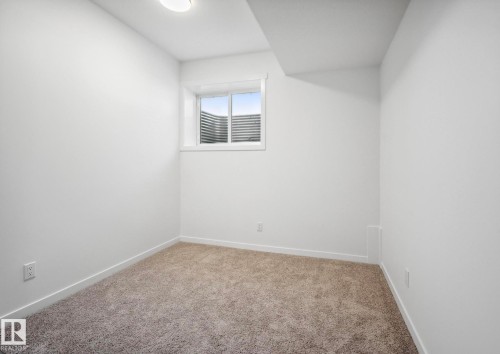 Bright interior room featuring a window with white trim, tan carpet flooring, white walls, and a flush-mount ceiling light - 3888 Wren Crescent, Edmonton, AB 