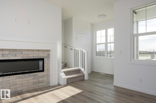 Living area featuring wood-finish flooring, a contemporary fireplace with light brick surround, and multiple windows providing natural light - 3888 Wren Crescent, Edmonton, AB 