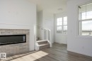 Living area featuring wood-finish flooring, a contemporary fireplace with light brick surround, and multiple windows providing natural light - 3888 Wren Crescent, Edmonton, AB 