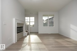 Living area featuring a built-in fireplace with a stone-finish surround, wood-finish flooring, white baseboards, and multiple windows - 