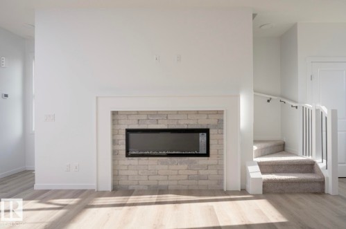 Modern electric fireplace with a light-toned brick surround, white mantel, and wood-finish flooring - 3888 Wren Crescent, Edmonton, AB 