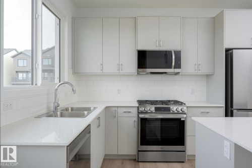 Modern kitchen with light grey cabinetry, white subway tile backsplash, and stainless steel appliances - 3888 Wren Crescent, Edmonton, AB 