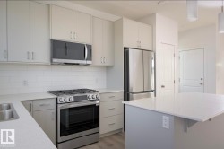 Modern kitchen featuring light gray cabinetry, stainless steel appliances, white subway tile backsplash, and light-toned countertops - 