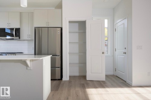 Modern kitchen featuring light cabinetry, stainless steel appliances, white subway tile backsplash, and a breakfast bar island with a white countertop - 3888 Wren Crescent, Edmonton, AB 