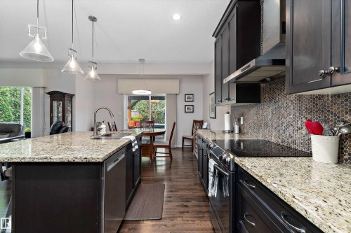 Modern kitchen featuring dark wood-finish cabinetry, light-toned granite countertops, and a full-height mosaic tile backsplash - 1097 Armitage Crescent, Edmonton, AB 