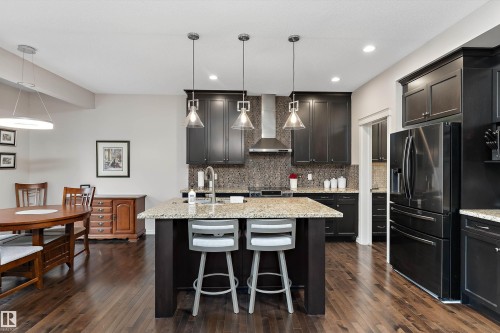 Gourmet kitchen featuring dark wood cabinetry, stainless steel appliances, granite countertops, a large center island with seating, and wood-finish flooring - 1097 Armitage Crescent, Edmonton, AB 