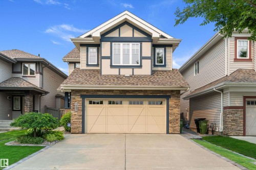 Two-story residence featuring a combination of stone veneer and siding facade, a two-car garage with a panel door, and multiple windows - 1097 Armitage Crescent, Edmonton, AB 