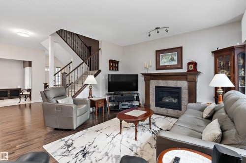 Spacious living area featuring wood-finish flooring, a traditional fireplace with a tile surround and wood mantel, and a staircase with dark wood newel posts and railings - 1097 Armitage Crescent, Edmonton, AB 