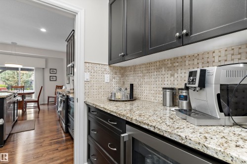 Modern kitchen with dark cabinetry, speckled countertops, patterned tile backsplash, and wood-finish flooring - 1097 Armitage Crescent, Edmonton, AB 