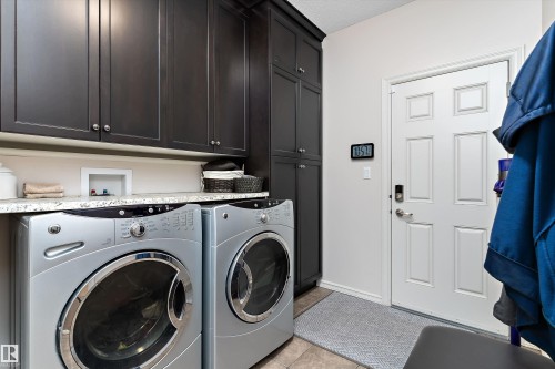 Dedicated laundry area featuring dark wood-finish cabinetry, a light-toned countertop, and tiled flooring - 1097 Armitage Crescent, Edmonton, AB 
