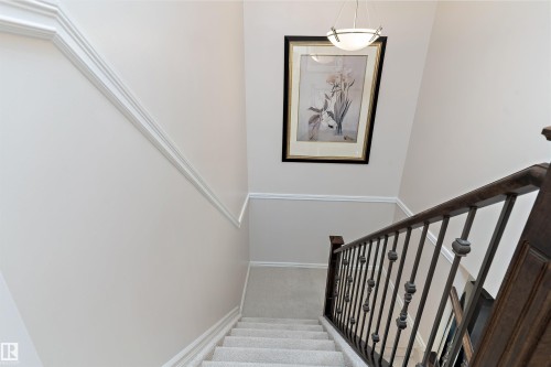 Carpeted staircase featuring a dark wood handrail with wrought iron balusters, white trim, and a high ceiling with a pendant light fixture - 1097 Armitage Crescent, Edmonton, AB 