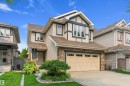 Two-story residence featuring light beige siding, dark blue trim, a stone façade, a two-car garage with carriage-style doors, and mature landscaping - 1097 Armitage Crescent, Edmonton, AB 