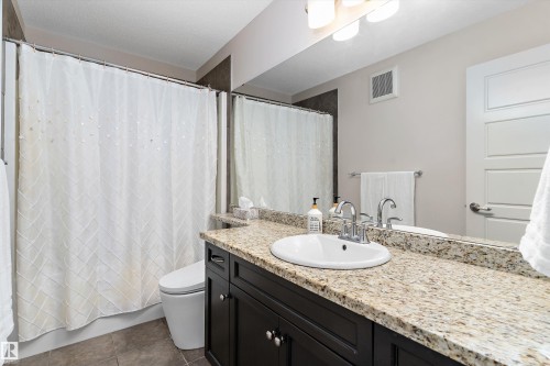 Bathroom featuring a dark wood vanity with a light granite countertop, an undermount sink, and chrome fixtures - 1097 Armitage Crescent, Edmonton, AB 