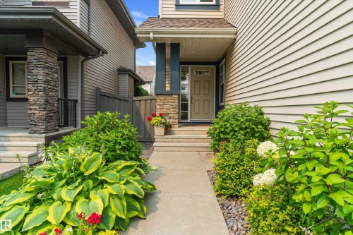 Front entryway featuring a stone veneer accent column, siding exterior, concrete pathway, and established landscaping - 1097 Armitage Crescent, Edmonton, AB 
