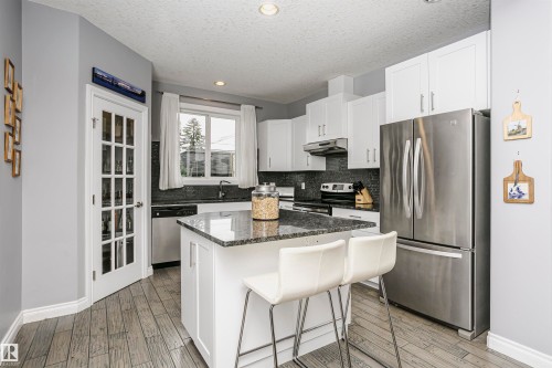 Kitchen featuring a central island with a dark granite-style countertop, white cabinetry, stainless steel appliances, and wood-finish flooring - 11619 125 Street, Edmonton, AB 
