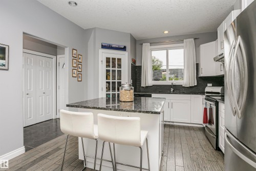Kitchen featuring an island with a stone countertop, white cabinetry, stainless steel appliances, wood-finish flooring, and a glass-paneled door - 11619 125 Street, Edmonton, AB 
