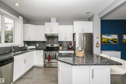 Kitchen featuring white cabinetry, dark speckled countertops, and stainless steel appliances - 11619 125 Street, Edmonton, AB 