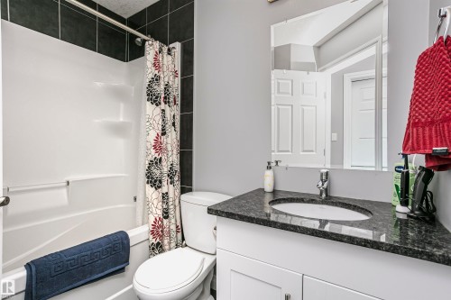 Bathroom featuring a white tub/shower combination, dark tile surround, a single vanity with a dark speckled countertop, and a contemporary wall mirror - 11619 125 Street, Edmonton, AB 