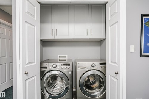 Dedicated laundry closet featuring a stackable washer and dryer, light gray cabinetry with brushed nickel hardware, and bifold doors - 11619 125 Street, Edmonton, AB 
